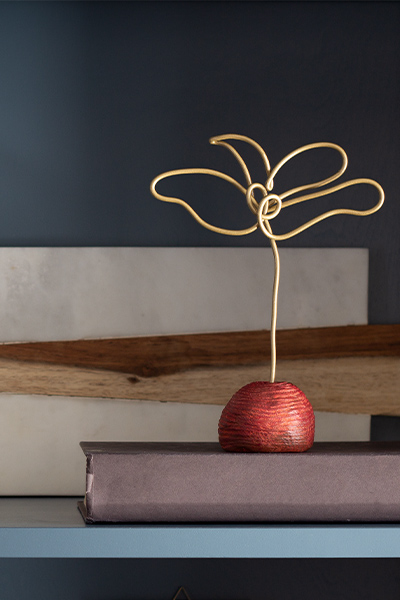 Gold wire sculpture with red base on a blue bookshelf